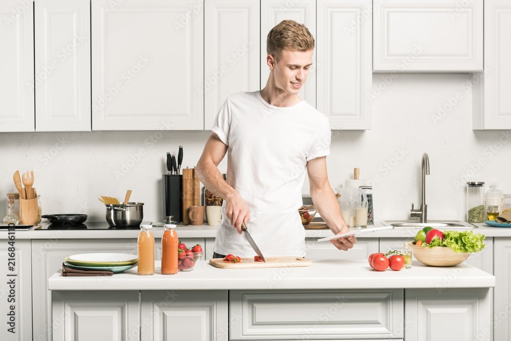 handsome young man cooking and reading recipe on tablet in kitchen handsome young man cooking and reading recipe on tablet in kitchen