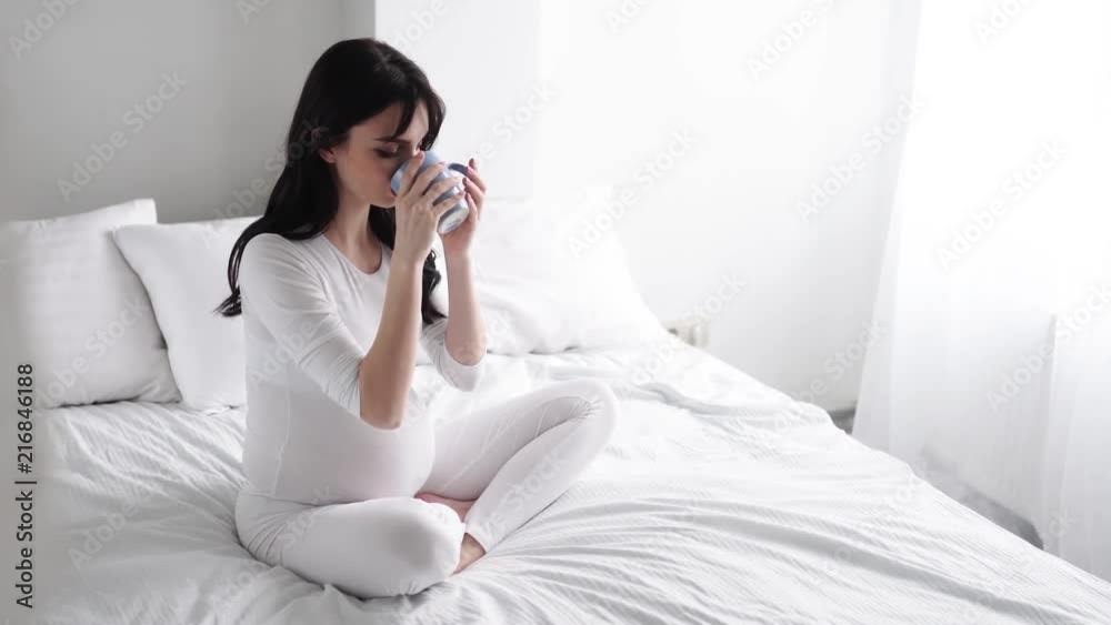 Pregnant Young Woman Drinking Tea And Sitting On Bed At Home Pregnant Young Woman Drinking Tea And Sitting On Bed At Home