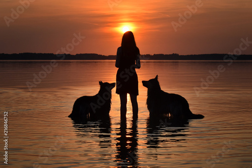 Dogs and girl watching sunset over a lake