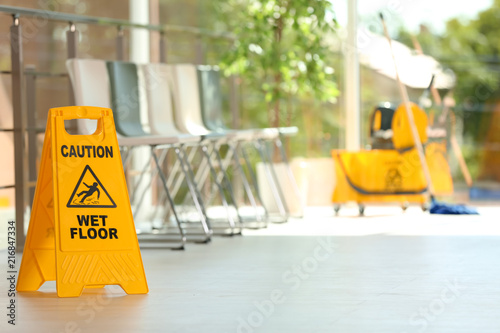 Safety sign with phrase Caution wet floor and blurred mop bucket on background. Cleaning service photo