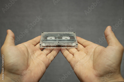 analog audio tape compact cassette in stretched palms on a gray empty background