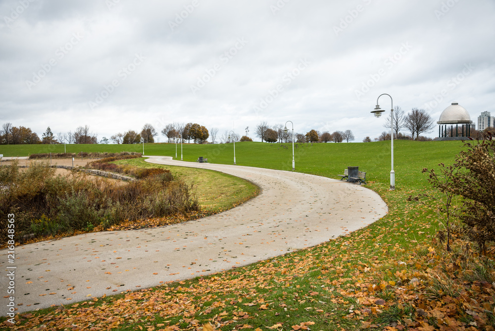 Winding Path in a Lakeside Park on a Cloudy Autumn Morning. Fallen Leaves are on Grass.