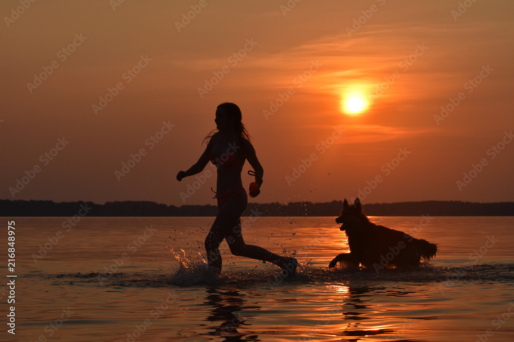 Girl and her dog running through a lake at sunset