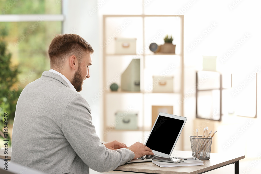 Young businessman using laptop at table in office