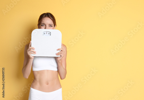 Happy slim woman satisfied with her diet results holding bathroom scales on color background