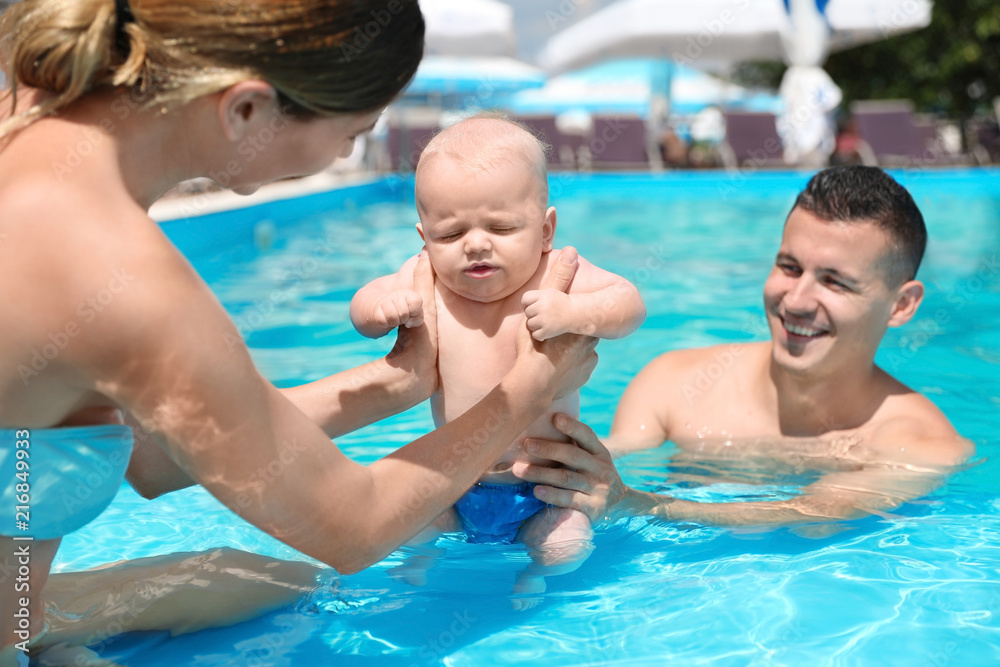 Happy parents with little baby in swimming pool on sunny day, outdoors Happy parents with little baby in swimming pool on sunny day, outdoors