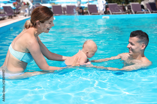 Happy parents with little baby in swimming pool on sunny day, outdoors © New Africa