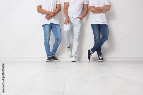 Group of young men in jeans near light wall