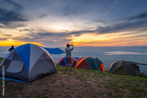 Camping outdoor man hiker taking photo with smart phone at mountain peak. camping vacation with sunrise landscape,camping over mountain for people love adventure lifestyle. Marvelous daybreak.