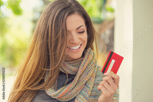 Cheerful excited young woman with credit card standing outdoors