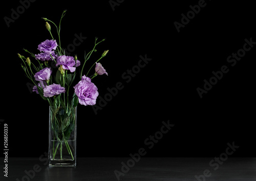 Vase with beautiful Eustoma flowers on table against dark background
