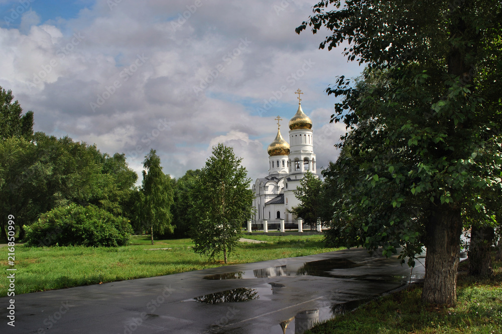 Christian orthodox temple with golden domes, trees and white clouds in the sky. Russia. Summer. After the rain.
