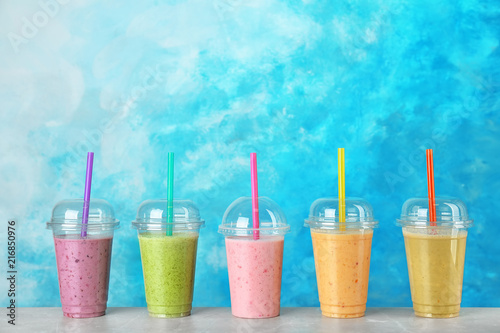 Plastic cups with smoothies on table against color background