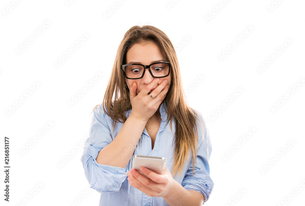 Stunned woman covering mouth and watching something on smart phone