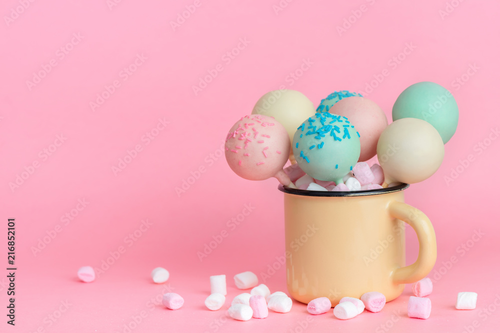 colorful glazed pop cakes and marshmallows in cup over pink background, concept of childrens party