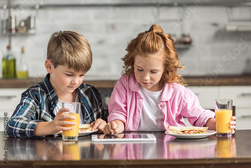 adorable little brother and sister using tablet during breakfast