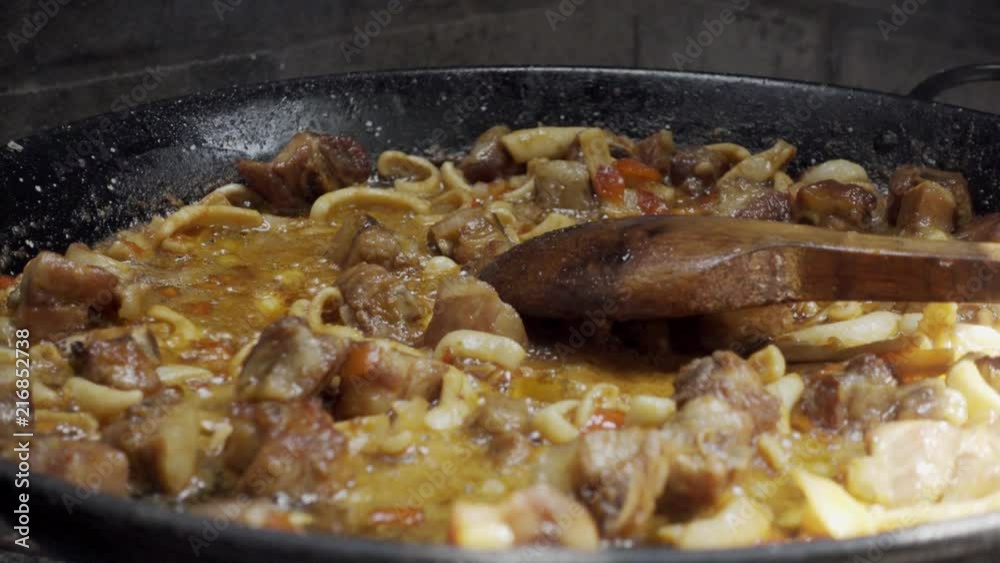 Zoom and pan close up of cooking Spanish paella, a famous typical spanish rice dish. Step one is to prepare a stir-fry with the onion, tomato, pieces of meat and sepia Zoom and pan close up of cooking Spanish paella, a famous typical spanish rice dish. Step one is to prepare a stir-fry with the onion, tomato, pieces of meat and sepia