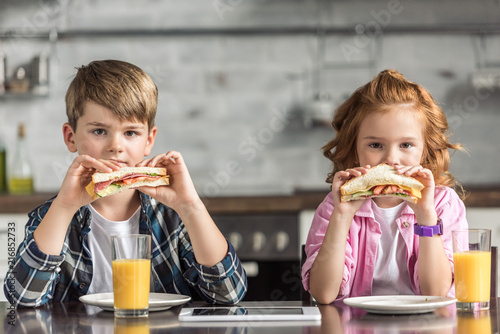 little brother and sister eating sandwiches and looking at camera