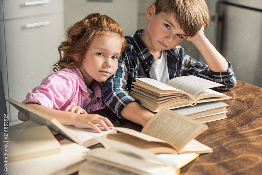 little brother and sister sitting at table with pile of books and looking at camera little brother and sister sitting at table with pile of books and looking at camera