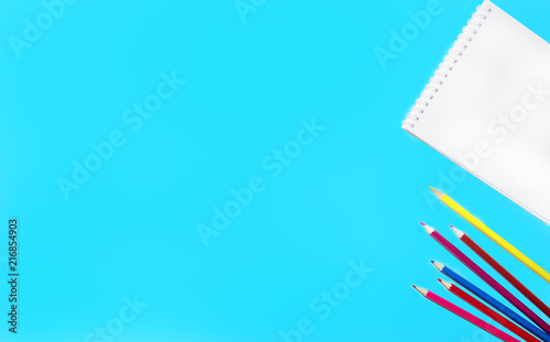 picture of colored pencils, notepad and scissors lined on a flat surface of an isolated blue background