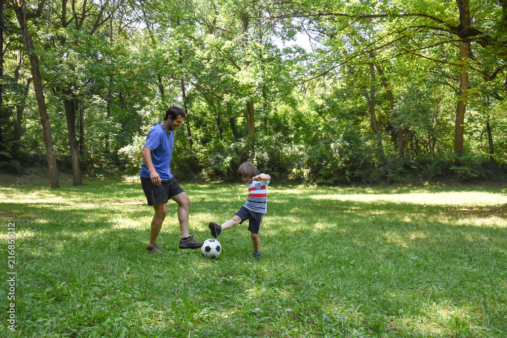 Father and son play with ball in autumn park. Happy family play soccer in public park