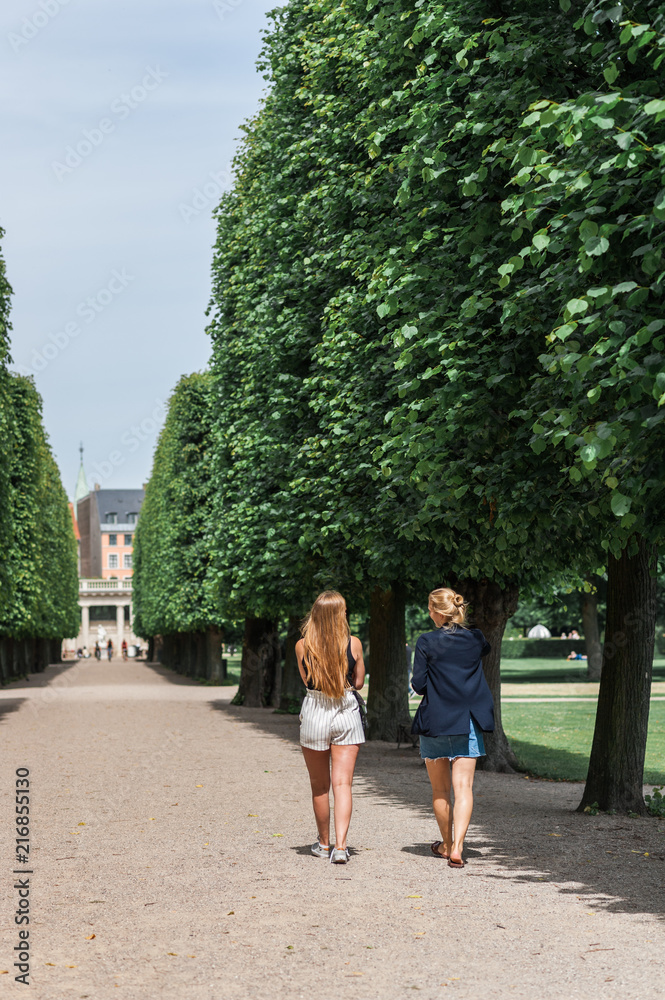 Obraz premium Young women relaxing during a summer day in a Danish park, perfectly manicured linden trees line an elegant garden alley. Concept of hygge.