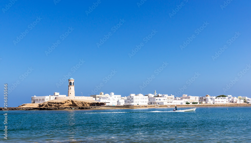View on Sur Lighthouse with fisherman boat passing - Sur, Oman