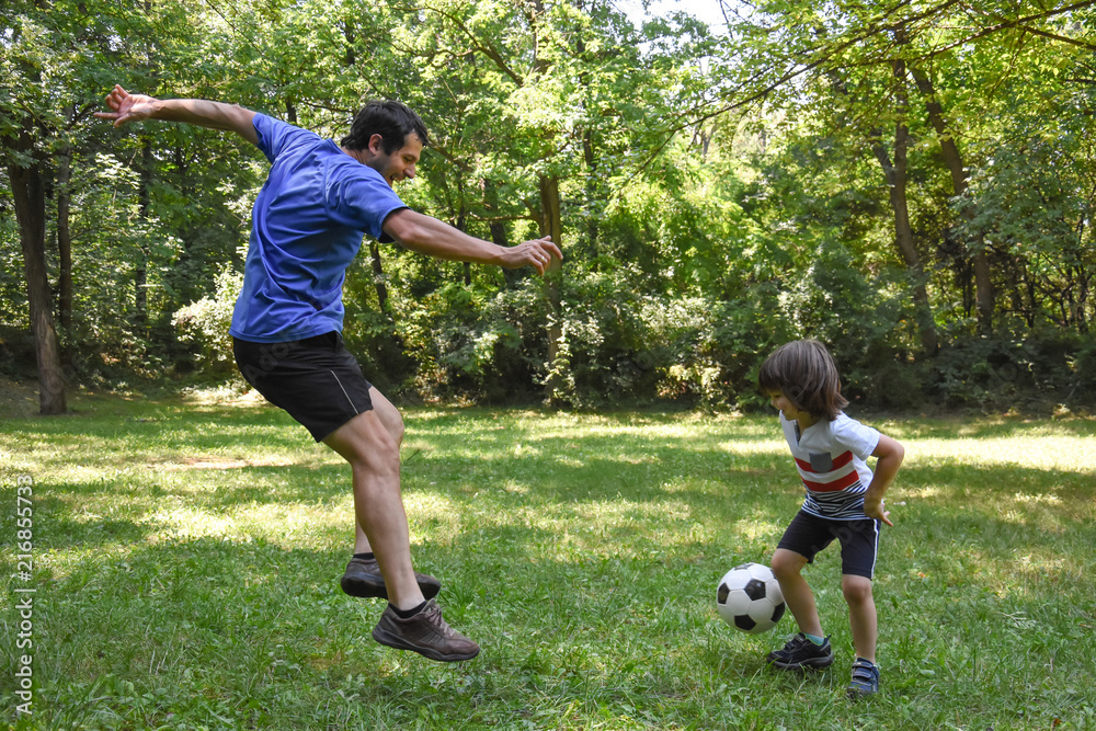 Father and son play with ball in autumn park. Happy family play soccer in public park Father and son play with ball in autumn park. Happy family play soccer in public park