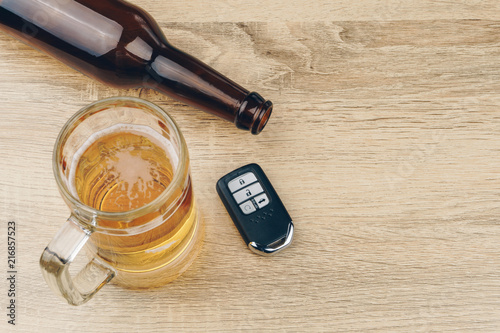 do not drink and drive concept, close up of a mug of beer and an empty beer bottle with a remote car key on wooden table