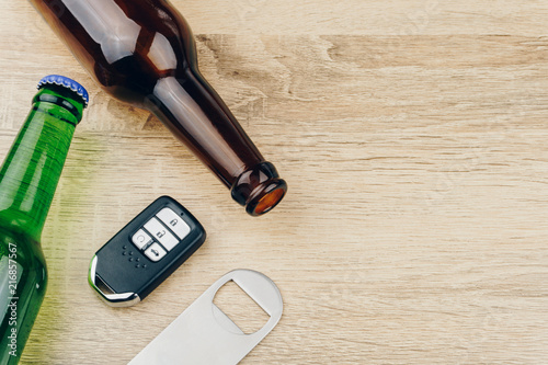 do not drink and drive concept, two bottles of beer and a remote car key with a stainless steel bottle opener or bar blade on wooden table