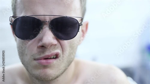 young man in sunglasses impulsively jerks his eyebrows and lip edge. mimic nervous tic. photo