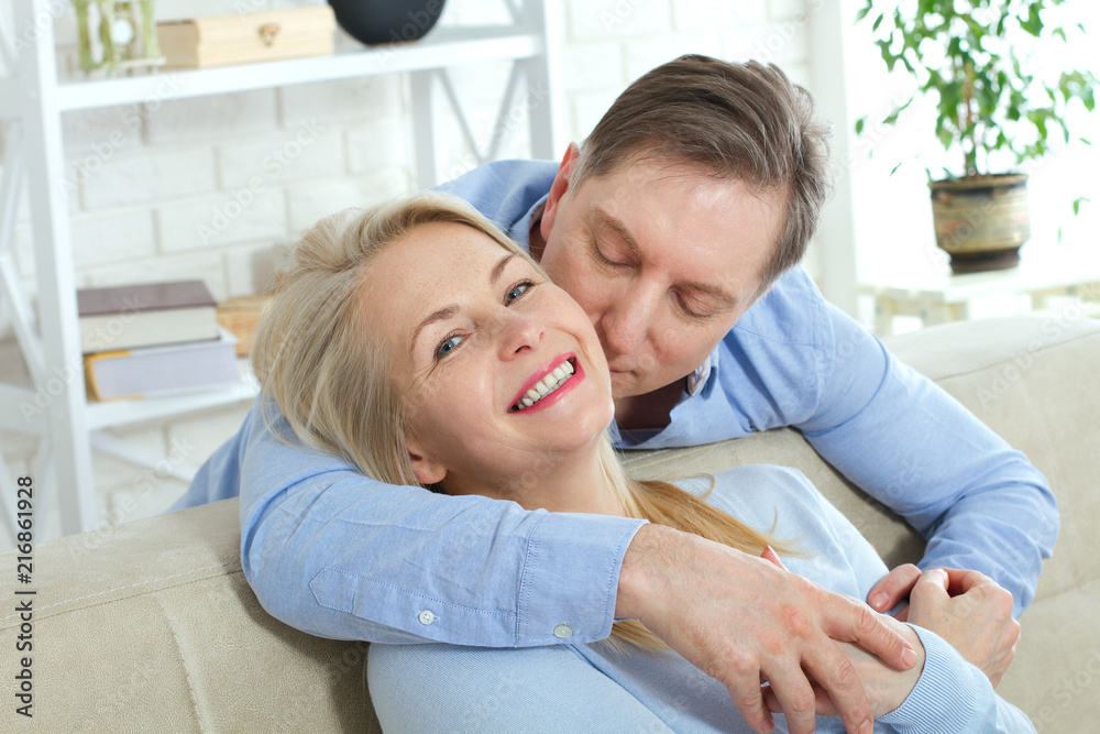 Close up photo of cheerful excited happy happily happy with toothy shining smile blond attractive woman and man, he hugs her from behind and kisses Close up photo of cheerful excited happy happily happy with toothy shining smile blond attractive woman and man, he hugs her from behind and kisses