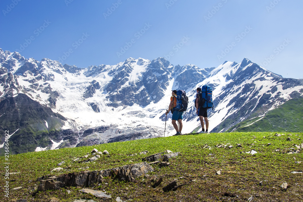 Hikers look at mountain range on a sunny summer day. Tourists in the highlands. Hiking in the mountains. Active trip to the beautiful nature. Leisure. Men on mountain trek. People in Caucasus Svaneti.