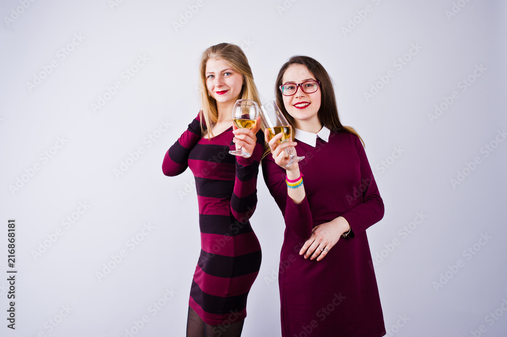 Two attractive friends in purple dresses drink sparkling wine or champagne in the studio. Two attractive friends in purple dresses drink sparkling wine or champagne in the studio.