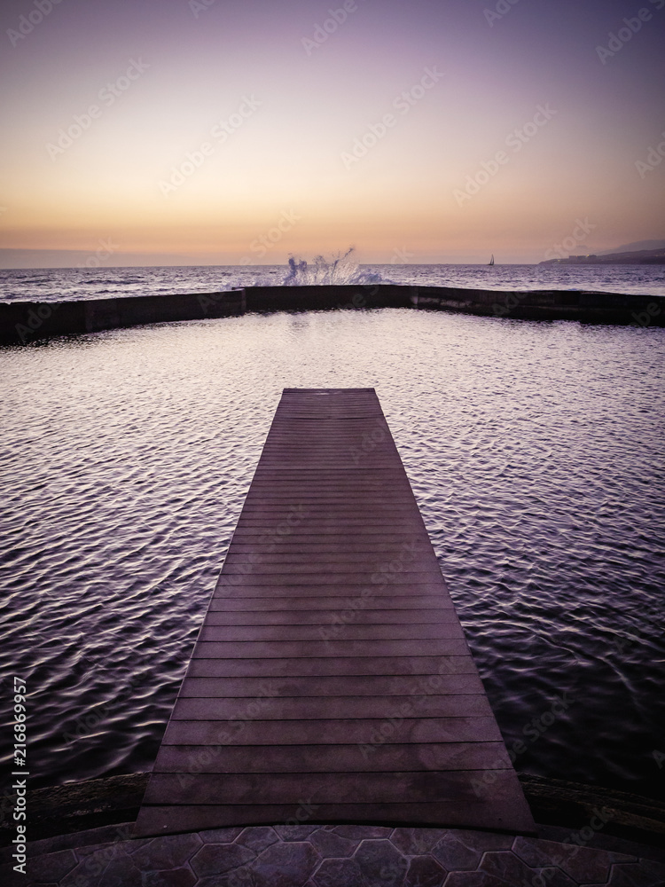 Obraz premium Jetty leading to the ocean at dusk with waves splashing against the sea wall in Tenerife