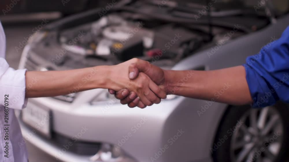 Close Up shot of mechanic and customer shaking hands in an auto repair shop, car service concept. Close Up shot of mechanic and customer shaking hands in an auto repair shop, car service concept.