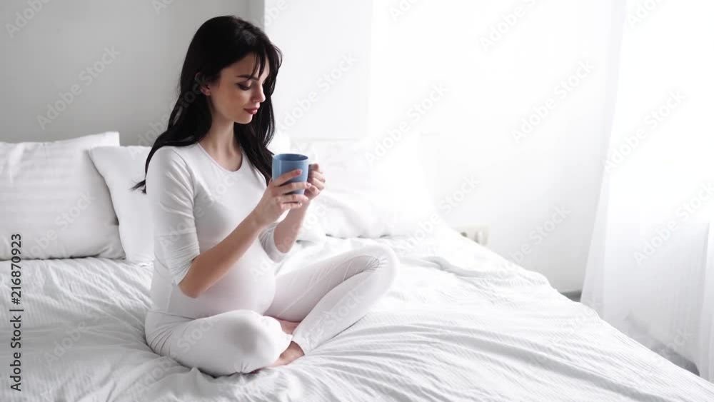 Pregnant Young Woman Drinking Tea And Sitting On Bed At Home Pregnant Young Woman Drinking Tea And Sitting On Bed At Home