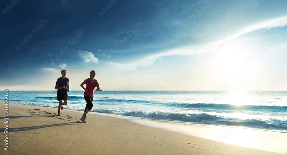 Man and women running on tropical beach at sunset