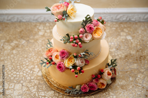 A close-up of a wedding cake is a gold color three-tiered. The festive cake from the confectioner is decorated with fresh flowers.