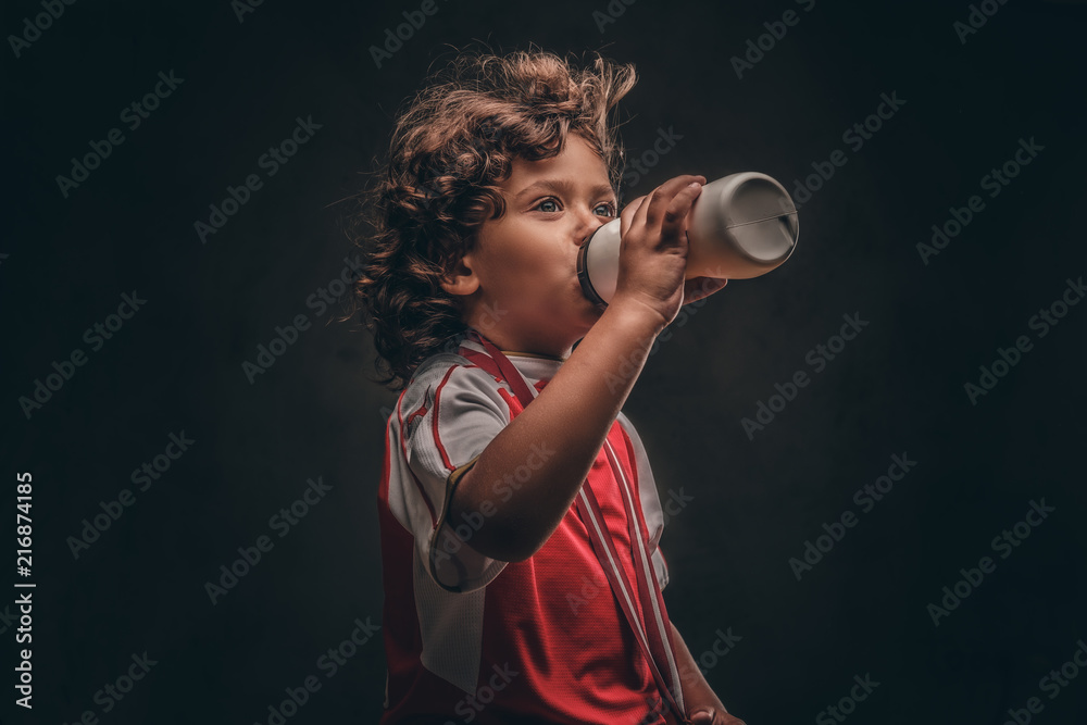 Little champion boy in sportswear with a gold medal drinking water from a  bottle. Isolated on a dark textured background. Stock Photo | Adobe Stock