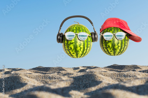 Creative and summer photography of watermelon in the form of a human head with glasses and red cap in the sand on the beach. Concept