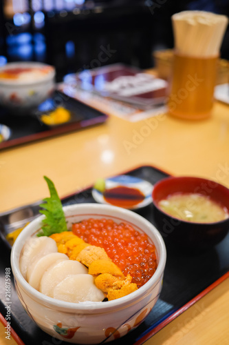 Tasty and delicious Sushi Donburi or Japanese rice bowl topped with fresh Sashimi Hotate(scallop),Ikura(salmon roe) and Uni(Sea Urchin) with Wasabi at a restaurant. Healthy Eating and Eat Well Concept