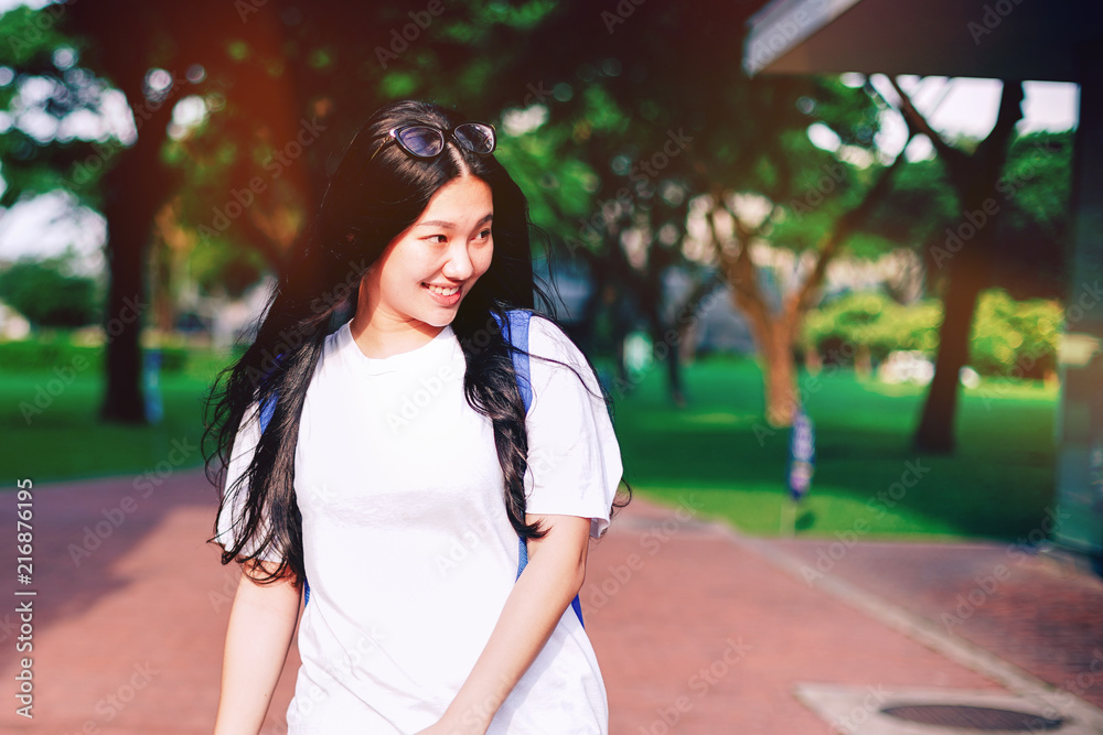 Fototapeta premium Portrait shot of beautiful young Asian female high school student smiling outdoor with light leaks from the sun light in the campus