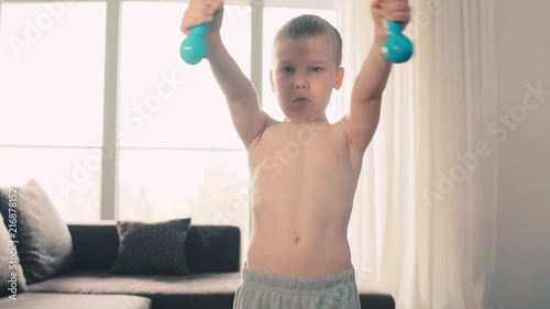 Happy child doing sports at home, boy fitness training dumbbells
