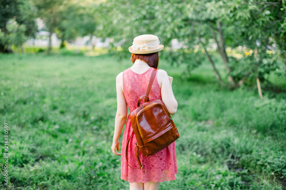 Obraz premium beautiful young woman in the garden. A girl in a straw hat. girl in a crimson dress with a leather backpack