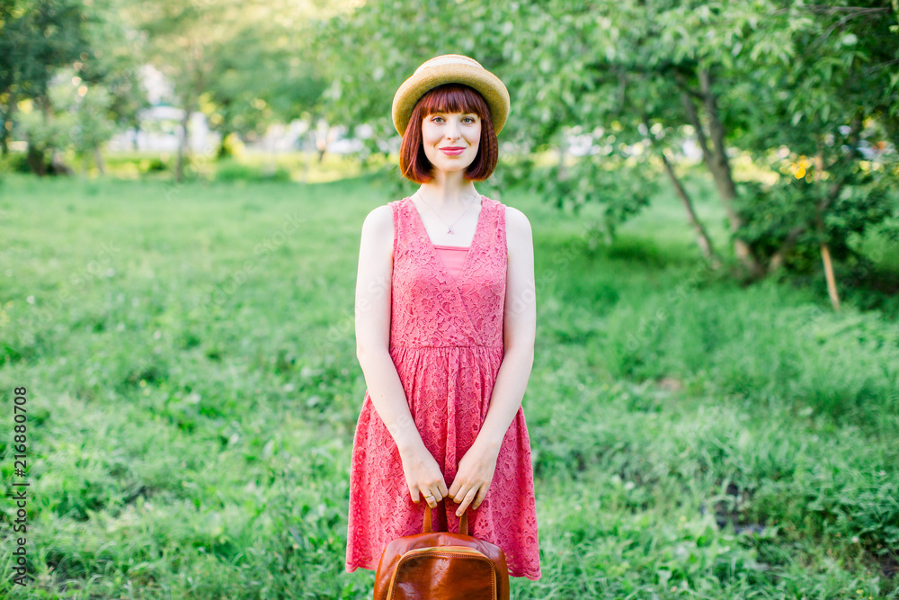 Obraz premium beautiful young woman in the garden. A girl in a straw hat. Portrait of a girl in a crimson dress smiles