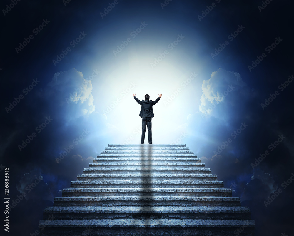 A man in a suit with arms outstretched on a stone staircase to the clouds and light. Stairway to Heaven.