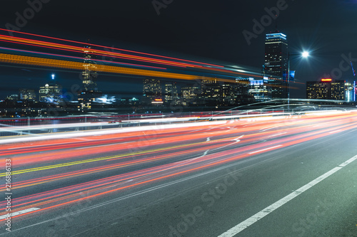 Boston skyline at night viewed from the Harvard Bridge in Boston, with light trails from cars and buses