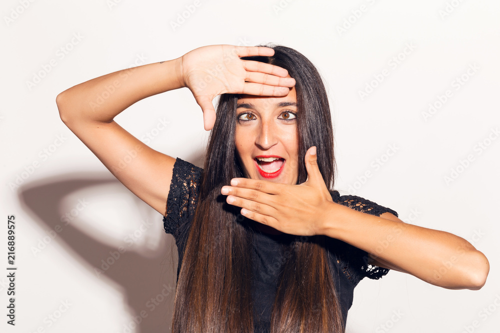 Fototapeta premium Young adult woman framing her face with her hands, making funny faces. In studio over a white background.