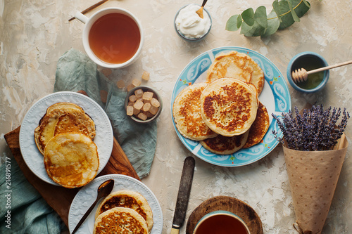 Tea, homemade pancakes, honey, cream sauce and lavender on light concrete table, romantic breakfast pancake party, various morning food, healthy lifestyle. Selective focus, top view © Irina